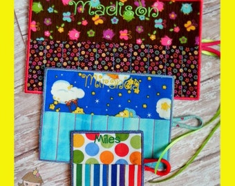 May include: Three personalised fabric items with embroidered names: "Madison" on a brown floral background, "Miranda" on a blue sky design, and "Miles" on a colourful polka dot and striped pattern. Each item has a different design and colour scheme.