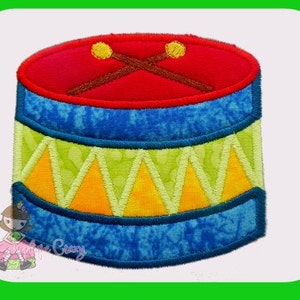 May include: A red, blue, yellow and green felt toy drum with two brown drumsticks. The drum has a blue and white patterned design.