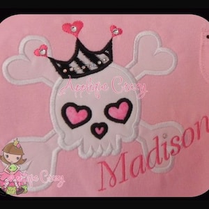 May include: Pink embroidered skull with a crown and pink hearts for eyes. The skull is part of a larger design that includes the word "Madison" in pink embroidery.
