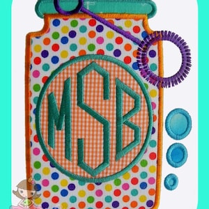 Może przedstawiać: Haftowany wzór przedstawiający słoik z kolorowym wzorem w kropki, pałeczkę do baniek mydlanych i monogram w kółku. Monogram to "MSB" w kratkę w kolorze zielonym i pomarańczowym.