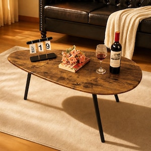 May include: Oval coffee table with a distressed wood finish and black metal legs. A bottle of red wine, a wine glass, and a small bouquet of flowers are on the table. A black desk calendar displays "MAY 19".