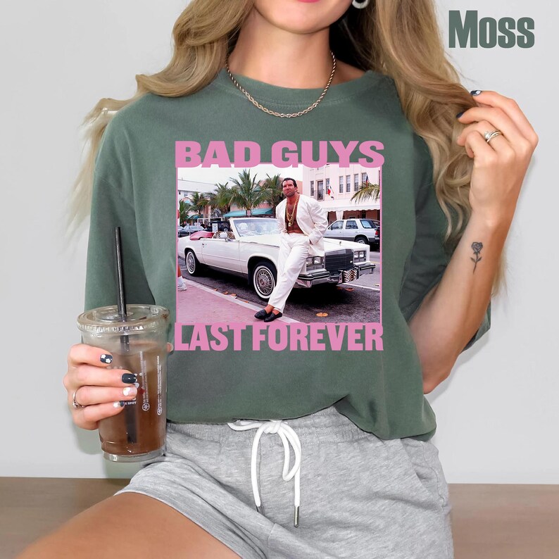 May include: Moss green t-shirt with a graphic featuring a man in a white suit leaning on a white convertible car. The text "BAD GUYS" and "LAST FOREVER" are in pink letters.