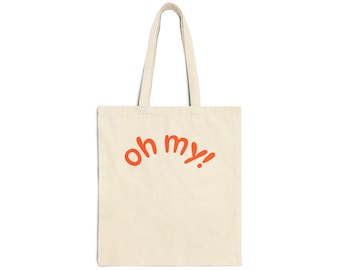 May include: A natural-colored canvas tote bag featuring two long shoulder straps and the text "oh my!" printed in a bold, orange, rounded font across the center of the bag. The design is simple, with the text arched slightly upward.
