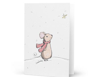 May include: A greeting card featuring a hand-drawn illustration of a small tan mouse wearing a pink scarf with white dots. The mouse stands on a snowy white ground looking up at a single gold star in the sky while light snow falls around it.