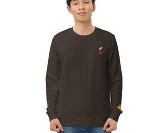 May include: A dark brown long-sleeve crewneck sweatshirt featuring a small embroidered graphic of a white mouse wearing a red coat on the upper left chest, and a yellow cheese graphic on the right sleeve cuff, paired with blue denim jeans.