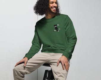 May include: A forest green crewneck sweatshirt featuring a small embroidered graphic on the left chest depicting a black and white cat silhouette with small white paw prints and circular accents surrounding the feline figure.