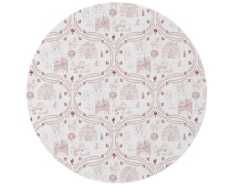May include: A round fabric mat featuring a repeating toile pattern in muted red on a white background. The design displays intricate line drawings of winter scenes, including small houses, trees, and deer, framed by curved, decorative borders.