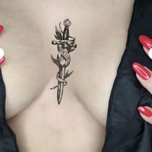 May include: A black and white tattoo of a sword with a banner that reads "Invictus" wrapped around it. The sword is adorned with leaves and is centered on the chest.