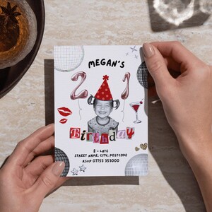 21st Birthday Invitation Template featuring a picture of a toddler wearing a party hat, balloons with a 2 and a 1, disco balls, scrapbook lettering, a cocktail, disco balls, lipstick kisses, sparkles, leopard print hearts and black text with the event details. The invite is being held on a desk, next to two glasses and a pen.