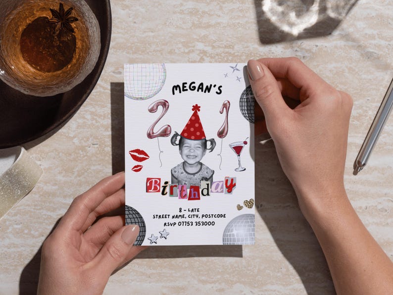 21st Birthday Invitation Template featuring a picture of a toddler wearing a party hat, balloons with a 2 and a 1, disco balls, scrapbook lettering, a cocktail, disco balls, lipstick kisses, sparkles, leopard print hearts and black text with the event details. The invite is being held on a desk, next to two glasses and a pen.