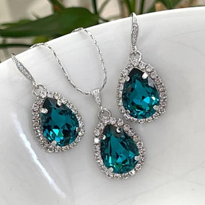 May include: A teal blue teardrop-shaped pendant necklace and matching earrings with a silver chain and clear crystal accents.