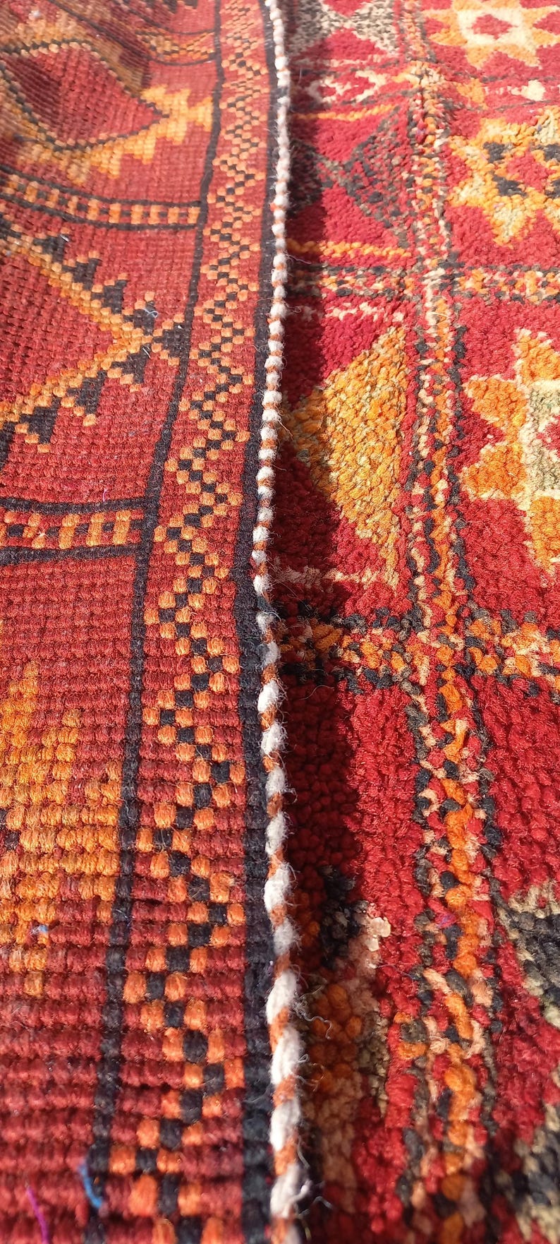 May include: Close-up of a section of a woven rug with a geometric pattern. The rug features a colour palette of red, orange, black, and white. The design includes repeating shapes and lines.