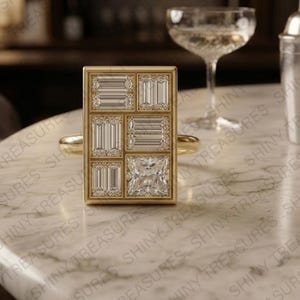 May include: A gold ring featuring a large rectangular face set with multiple baguette-cut diamonds and one square-cut diamond. The stones are arranged in a grid pattern within a polished gold frame, creating a geometric design on a smooth gold band.