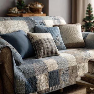 May include: A sofa with a patchwork quilt cover in shades of blue, cream, and brown. Several decorative throw pillows in various patterns and colors rest on the sofa. The scene evokes a cozy, rustic aesthetic.