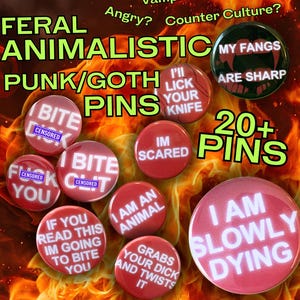 May include: A collection of round pin-back buttons featuring red and black backgrounds with white text. Phrases include I AM SLOWLY DYING, I AM AN ANIMAL, IM SCARED, I BITE, and MY FANGS ARE SHARP. The buttons are displayed against a fiery orange background.