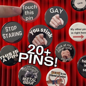 May include: A collection of circular pin-back buttons featuring various text and graphics, including phrases like 'pin layout is my passion', 'Touch this pin', 'GAY', 'STOP STARING', 'you stink', 'My other pin is right here', 'THIS IS A PIN', and 'METAL GEAR'.