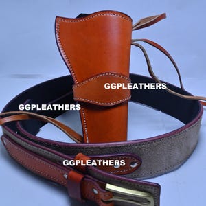 Op de afbeelding: Een bruin leren holster met bijpassende riem. Het holster is lichtbruin met witte stiksels en de tekst "GGLEATHERS". De riem is bruin met een suède middenstuk en een messing gesp.