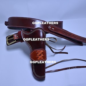May include: A brown leather holster and belt set. The holster is designed to hold a handgun and features a decorative stitched design. The belt has a brass buckle and is designed to be worn around the waist. The text "GGLEATHERS" is visible on the belt and holster.
