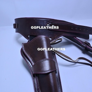 Puede incluir: Un conjunto de funda y cinturón de cuero marrón. La funda está diseñada para sujetar un arma de fuego y se fija a un cinturón. El texto "GGLEATHERS" es visible tanto en la funda como en el cinturón. El conjunto es de cuero marrón oscuro.
