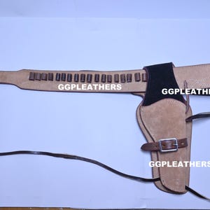 Może przedstawiać: Brązowy skórzany pas do broni i zestaw kabury. Pas posiada pętle na naboje i klamrę. Kabura jest przymocowana do paska i ma pasek z klamrą. Tekst "GGLEATHERS" jest wydrukowany.