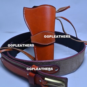 Może przedstawiać: Brązowa skórzana kabura z pasującym paskiem. Kabura jest w jasnobrązowym kolorze z białymi przeszyciami i napisem "GGLEATHERS". Pasek jest brązowy z zamszowym środkiem i mosiężną klamrą.