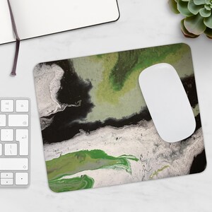 Peut inclure: Tapis de souris rectangulaire avec un motif abstrait dans les tons de vert, blanc et noir. Une souris d'ordinateur blanche est posée dessus. Le motif ressemble à un effet marbré ou d'art fluide, avec des couleurs tourbillonnantes.
