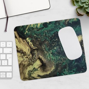 Peut inclure: Tapis de souris rectangulaire avec un motif abstrait dans les tons de vert, marron et jaune. Une souris d'ordinateur blanche repose sur le tapis. Un clavier et un bloc-notes sont visibles.