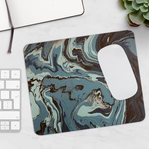 Peut inclure: Un tapis de souris rectangulaire avec un motif marbré dans les tons de bleu, marron et blanc. Une souris d'ordinateur blanche repose sur le tapis. Un clavier, un carnet et une plante succulente sont également visibles.