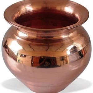 May include: A copper-coloured pot with a wide, flared rim and a rounded body. The polished surface reflects the surrounding environment. The pot's design features a smooth transition from the base to the rim, creating a classic, elegant look.