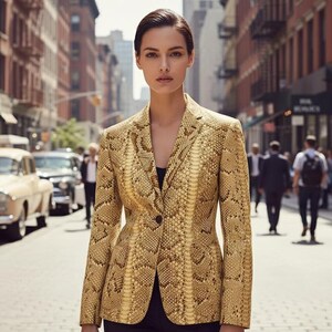 Könnte beinhalten: Ein goldfarbener Blazer mit Schlangenmuster. Der Blazer hat einen einzelnen schwarzen Knopfverschluss und ein klassisches Revers. Die Jacke wird über einem schwarzen Oberteil getragen. Der Hintergrund zeigt eine Stadtstraße mit Autos und Fußgängern.