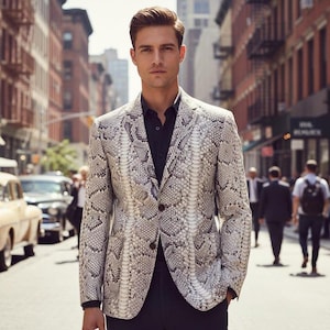 Könnte beinhalten: Ein hellfarbener Blazer mit Schlangenmuster. Die Jacke hat einen Zwei-Knopf-Verschluss und ein fallendes Revers. Die Person trägt ein schwarzes Hemd und eine schwarze Hose. Der Hintergrund ist eine Stadtstraße mit Gebäuden und Menschen.