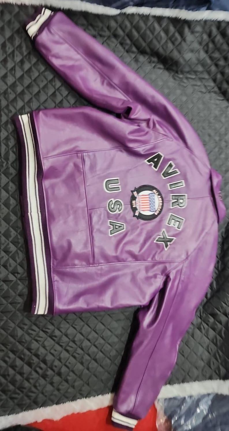 May include: A purple leather jacket with white and black striped cuffs and collar. The back of the jacket features the text "AVIREX USA" with a circular emblem. The jacket is made of a shiny material.