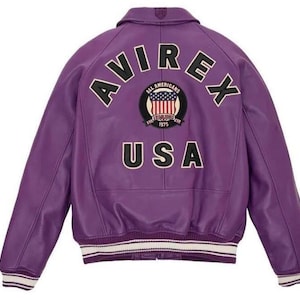 May include: A purple leather jacket with the word "AVIREX" arched across the shoulders. Below the word "AVIREX" is a patch with the words "ALL AMERICANS ESTABLISHED 1975" and a US flag design. The word "USA" is below the patch.