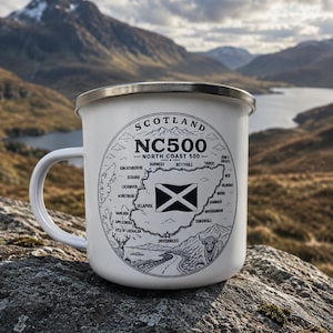 May include: White enamel mug with a map of Scotland's North Coast 500 route, labelled "SCOTLAND NC500". The mug has a silver rim and handle, and the design includes a Scottish flag, road, and illustrations of a deer and a bull.