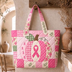 May include: A quilted tote bag featuring a central pumpkin appliqué with a pink breast cancer awareness ribbon. The bag is constructed from various pink and white fabric patches, including gingham, polka dot, and floral patterns, with two handles.