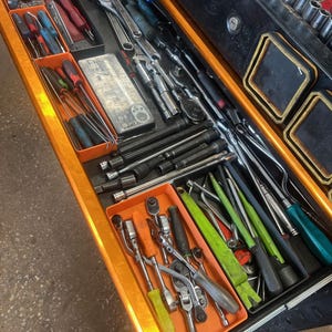 May include: An open toolbox drawer filled with various hand tools. The tools include screwdrivers, wrenches, ratchets, sockets, and pry bars. The drawer is orange and black, with the tools neatly organized in orange trays.