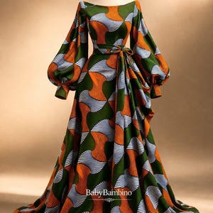 May include: A long, flowing dress with a vibrant geometric pattern in shades of green, orange, and white. The dress features long, voluminous sleeves and a cinched waist with a matching tie. The text "BabyBambino" is visible on the dress.