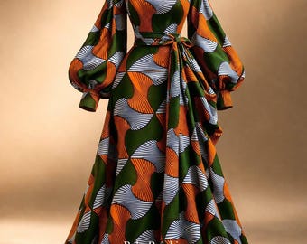 May include: A long, flowing dress with a vibrant geometric pattern in shades of green, orange, and white. The dress features long, voluminous sleeves and a cinched waist with a matching tie. The text "BabyBambino" is visible on the dress.