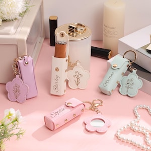 Può includere: Una collezione di porta rossetti personalizzati in vari colori pastello, tra cui rosa, lavanda e verde menta. Ogni porta rossetto ha un portachiavi a forma di fiore abbinato con un design floreale. Alcuni porta rossetti sono etichettati con nomi come "Shirley" e "Sophie".