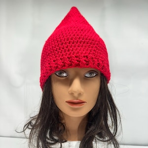 May include: A vibrant red, handmade crochet hat with a conical crown. The hat is crafted from a chunky yarn, giving it a textured look. The hat is displayed on a mannequin head with dark hair.