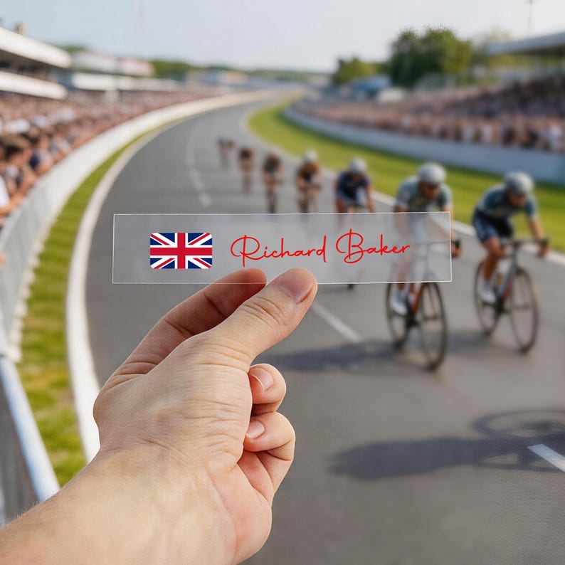 May include: A clear rectangular name tag with the Union Jack flag and the name "Richard Baker" in red script. The background shows a bicycle race on a track.