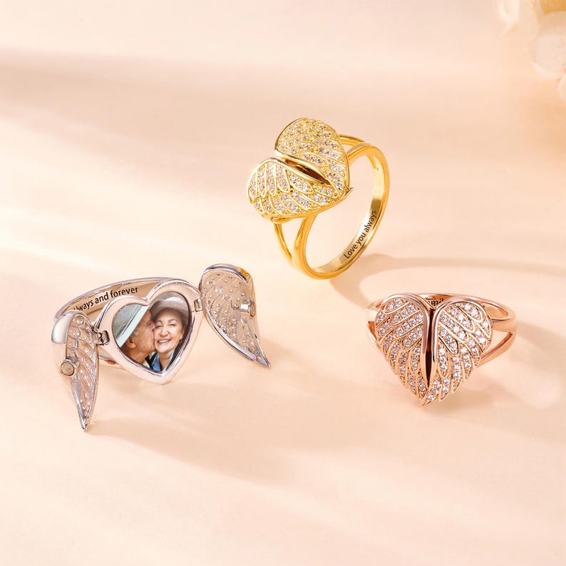 May include: Three rings with heart and wing designs. One is silver with a photo inside and the words "ways and forever". Another is gold with "Love you always" inscribed. The third is rose gold.