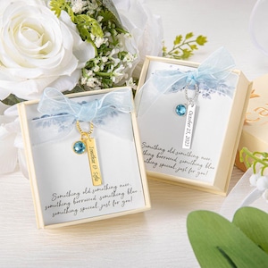 May include: Two gift boxes with a gold-colored necklace and a blue gemstone pendant. Each box has a light blue ribbon and the text "Something old something new..." The necklace has a tag with the names "Jonathan & Sofia" or the date "October 25, 2023".