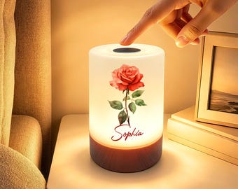 May include: A cylindrical table lamp with a white frosted shade featuring a red rose illustration and the name Sophia printed in red script. The lamp has a dark wood-grain base and a circular touch-sensitive power button on the top surface.