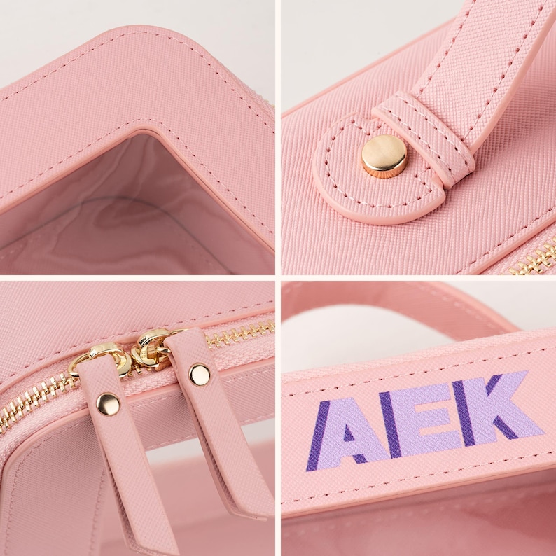 May include: A pink cosmetic bag with a clear window and gold-colored zipper. The bag has a handle with the letters "AEK" in purple. The bag is made of a textured material.