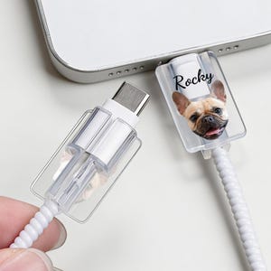 May include: White charging cable with a clear plastic protector. One protector features a French Bulldog image and the name "Rocky". The cable is connected to a device, suggesting a tech accessory.