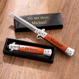 Peut inclure: Deux couteaux à cran d'arrêt personnalisés avec manches en bois, un ouvert et un fermé, gravés des noms "Michael" et "Jackson". Les couteaux sont dans des boîtes noires avec le texte "TO MY MAN Michael".