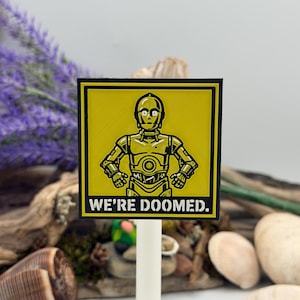 May include: A square yellow sign featuring a black graphic illustration of the robot C-3PO with the text WE'RE DOOMED. printed in black at the bottom. The sign is mounted on a thin white vertical post and has a black border.