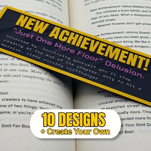 May include: A rectangular bookmark with a yellow border and dark background featuring the yellow text NEW ACHIEVEMENT! and purple text Just One More Floor Delusion. The text continues with Unlocked by: Convincing yourself you'll stop reading at the end of the chapter, only to hit a massive, sleep-ruining cliffhanger. A white label below reads 10 DESIGNS + Create Your Own.