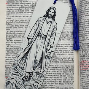 May include: A white rectangular bookmark featuring a black and white ink illustration of a bearded figure in robes walking on water. The bookmark has a rounded top with a hole and a vibrant blue silk tassel attached to the top center of the object.